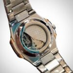 Two-tone stainless steel skeleton watch with gold bezel, silver bracelet, and exposed automatic movement.