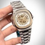 Two-tone stainless steel skeleton watch with gold bezel, silver bracelet, and exposed automatic movement.