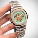 Two-tone stainless steel skeleton watch with gold bezel, silver bracelet, and exposed automatic movement.