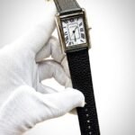 Silver rectangular tank-style watch with white dial, black Roman numerals, and brown leather strap.