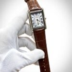 Silver rectangular tank-style watch with white dial, black Roman numerals, and brown leather strap.