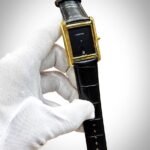 Silver rectangular tank-style watch with white dial, black Roman numerals, and brown leather strap.