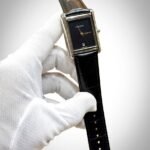 Silver rectangular tank-style watch with white dial, black Roman numerals, and brown leather strap.