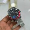 Silver-tone GMT style watch with black dial, red and black bezel, luminous markers, and jubilee bracelet held in hand.