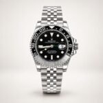 Silver-tone GMT style watch with black dial, black and blue rotating bezel, and jubilee bracelet held in hand.