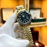 Gold-tone GMT style watch with black dial, black and grey bezel, and gold jubilee bracelet.