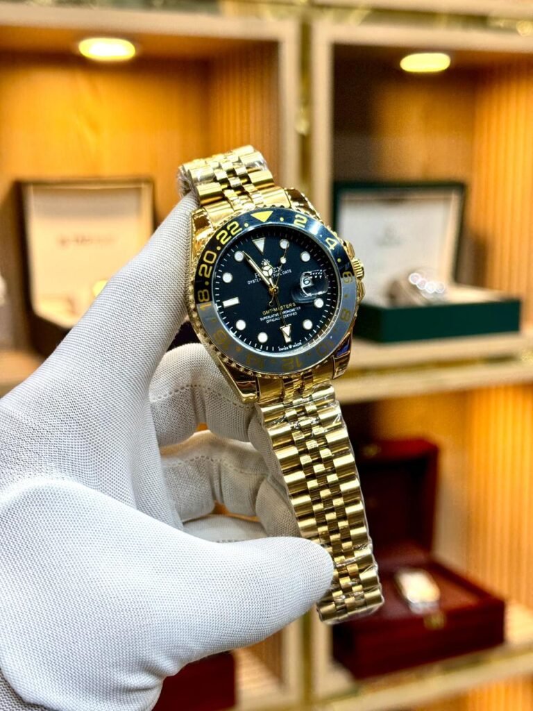 Gold-tone GMT style watch with black dial, black and grey bezel, and gold jubilee bracelet.