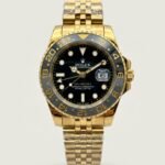 Gold-tone GMT style watch with black dial, black and grey bezel, and gold jubilee bracelet.