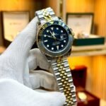 Two-tone silver and gold GMT style watch with black dial, black and grey bezel, and two-tone jubilee bracelet.
