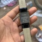 Silver rectangular dress watch with white dial, black Roman numerals, blued-steel hands, and brown leather strap.