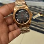 Premium rose gold automatic day-date watch with black Roman numeral dial, fluted bezel, and rose gold president bracelet.